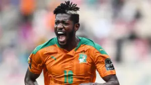 Ibrahim Sangaré celebrating in an orange Ivory Coast football kit during a match.