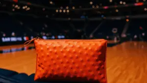 Orange clutch bag courtside at NBA arena under bright stadium lights