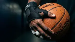 Basketball player's hand in protective brace gripping basketball with dramatic lighting