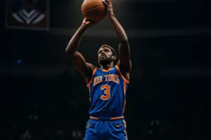 Knicks player shooting three-pointer at Madison Square Garden with championship banners visible