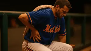 Mets player on dugout bench with hand on lower back showing injury discomfort during game