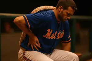 Mets player on dugout bench with hand on lower back showing injury discomfort during game