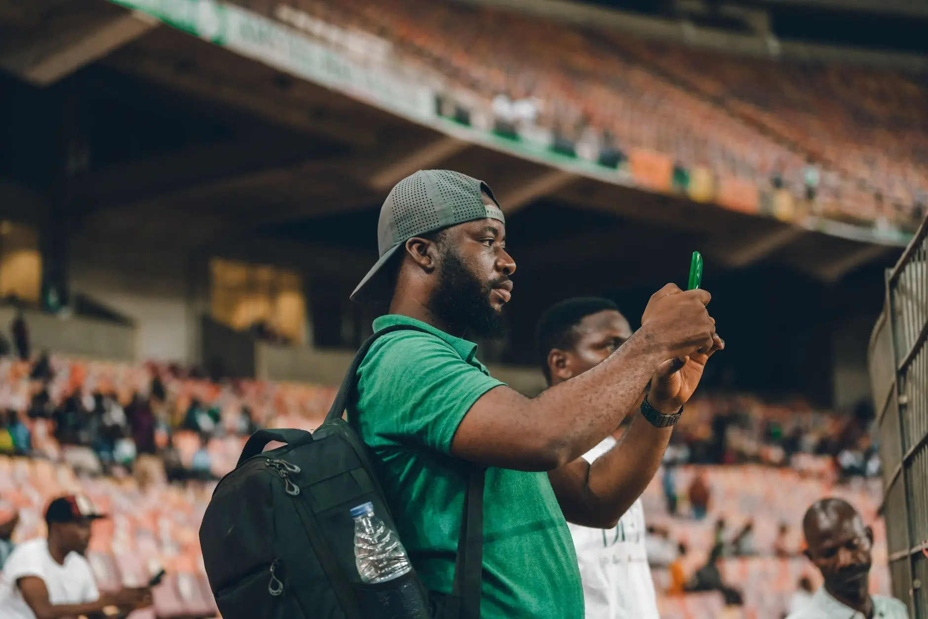 Man in a green shirt using a smartphone at a stadium.
