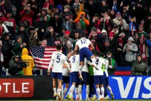 USMNT soccer fans celebrate a goal with an American flag in the crowd.