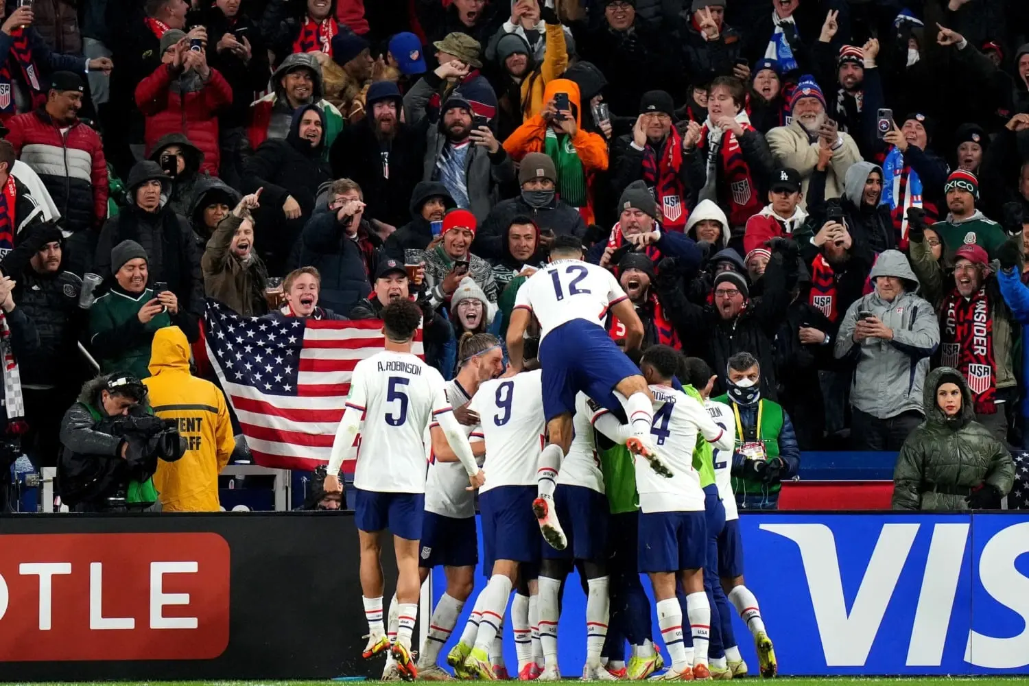 USMNT soccer fans celebrate a goal with an American flag in the crowd.