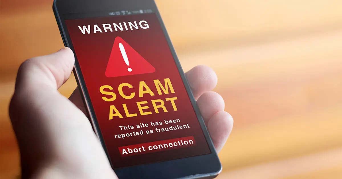 Hand holding a smartphone displaying a scam alert warning.