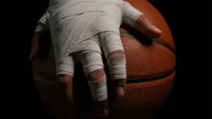 Injured basketball player's taped hand gripping basketball in dramatic lighting