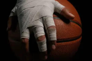 Injured basketball player's taped hand gripping basketball in dramatic lighting
