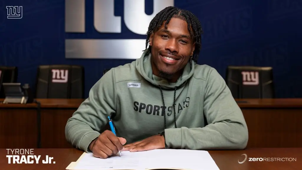 Tyrone Tracy Jr. smiling while signing papers at a Giants table.