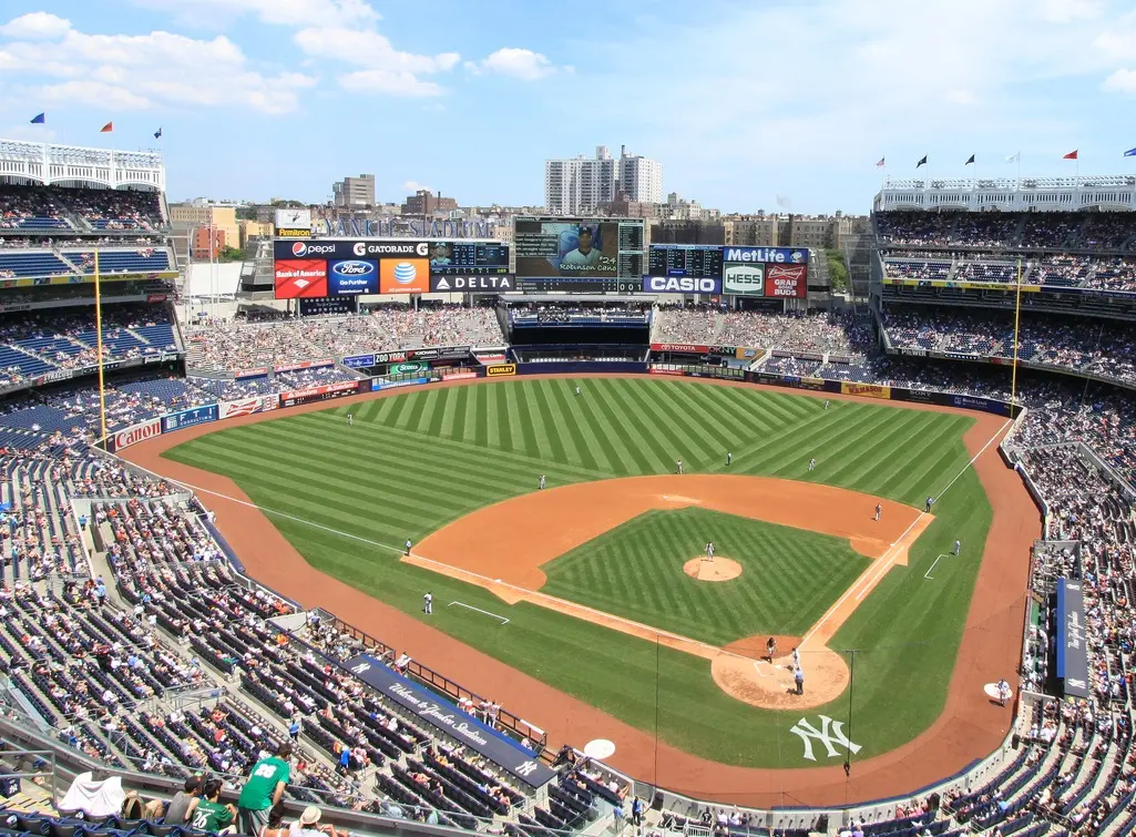 A panoramic view of Yankee Stadium baseball field showing fans, players, and scoreboard.